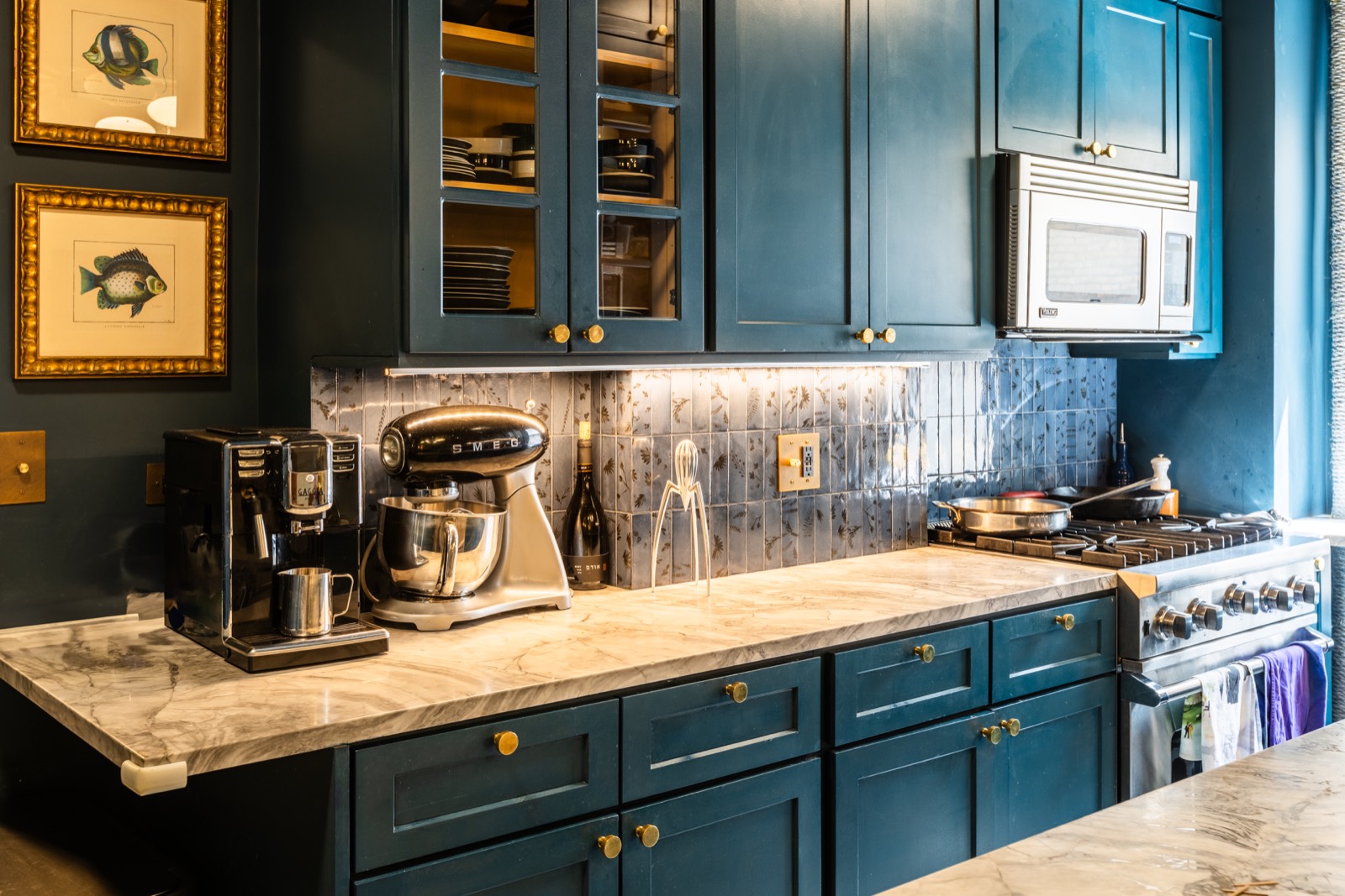 Blue kitchen cabinetry with marble counter, tile backsplash, and brass hardware