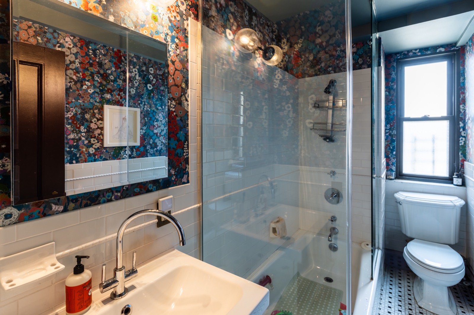 Bathroom with floral wallpaper, glass shower, and white tile