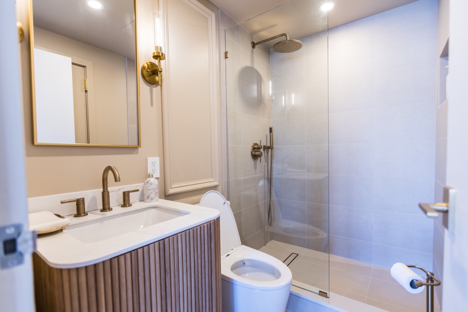 Bathroom with fluted wood vanity, brass fixtures, and glass shower