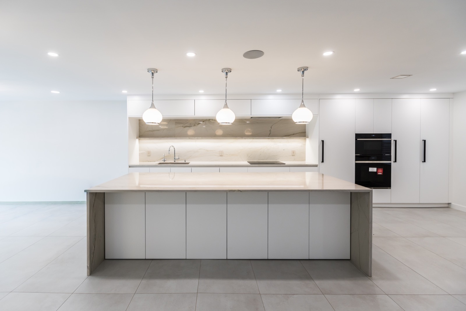 Minimal white kitchen with large island, pendant lighting, and integrated appliances