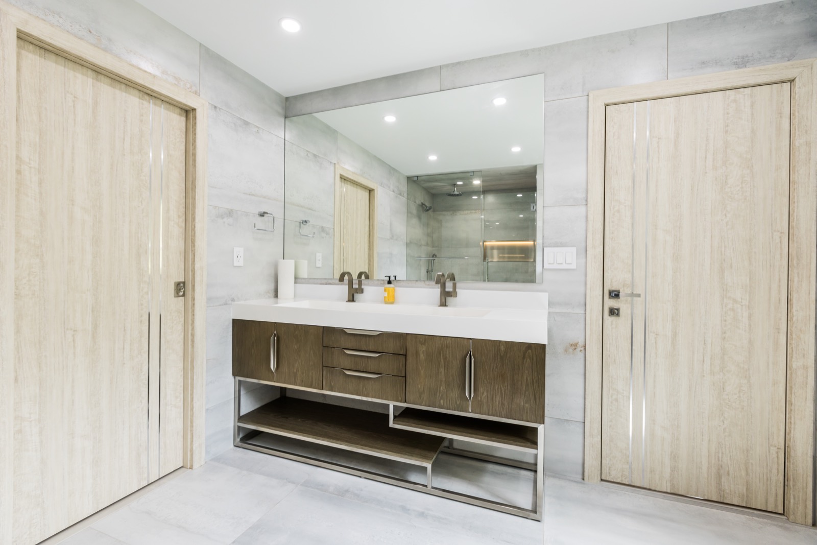 Modern bathroom vanity with large mirror, stone tile, and wood doors