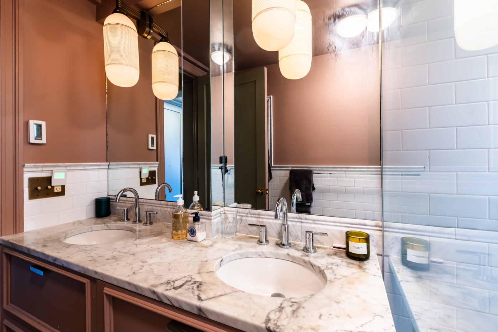 Pink bathroom vanity with marble counter, mirror, and glass shower