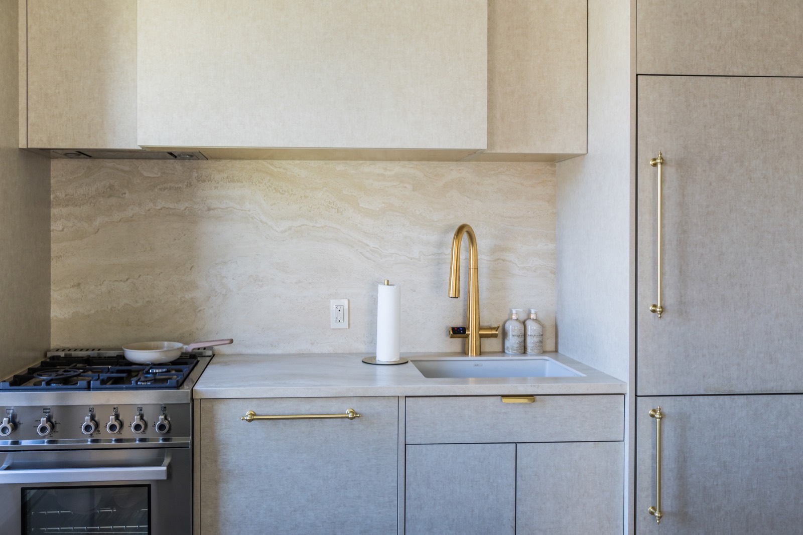 Kitchen detail with stone backsplash, brass faucet, and integrated cabinetry