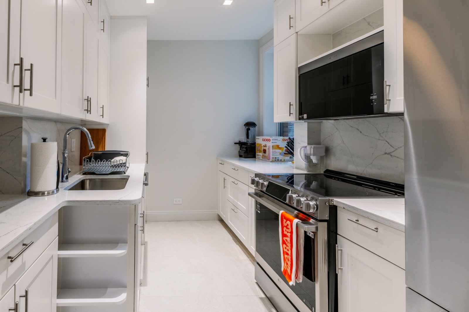 White galley kitchen with stone backsplash and stainless appliances