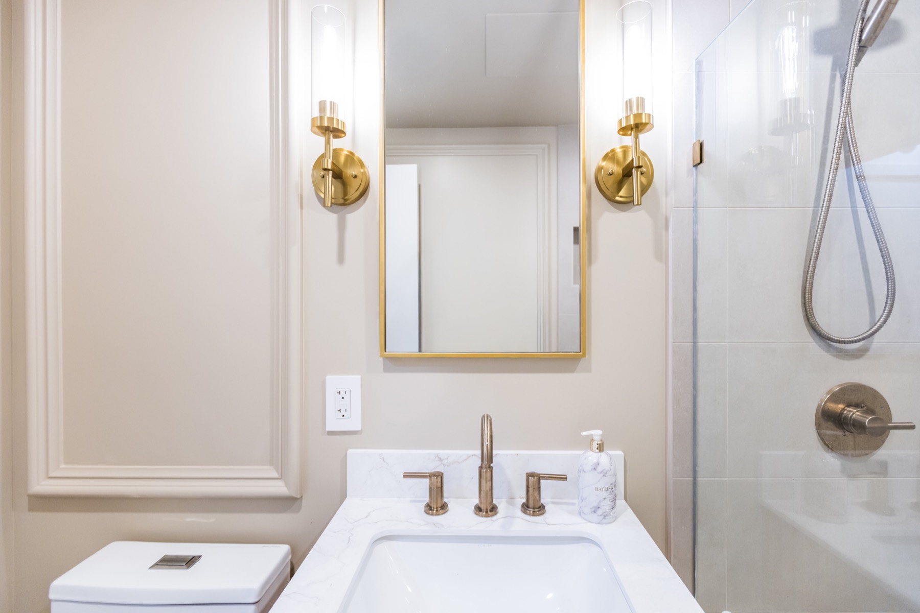 Luxury bathroom vanity renovation with brass mirror lighting and glass shower by Build in NYC